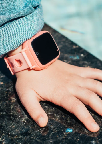 Közeli kép egy gyermek kezéről, melyen egy rózsaszín okosóra látható, sötét, márványos felületen fekve. Okosóra, gyerek okosóra, digitális eszköz, technológia, biztonság, követés, távfelügyelet, gyermekvédelem, viselhető technológia.